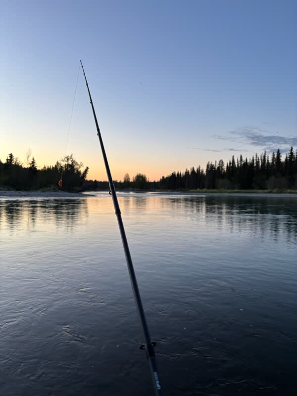 Fishing rod over calm Alaska water at sunset